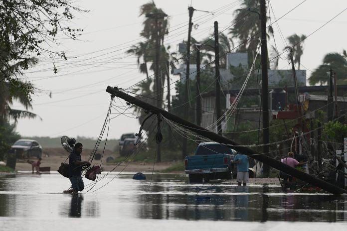 A man carries items through floodwater past downed electric lines after the passing of Hurricane Polo in Puerto San Carlos, Baja California Sur state, Mexico, Tuesday, Sept. 29, 2026.