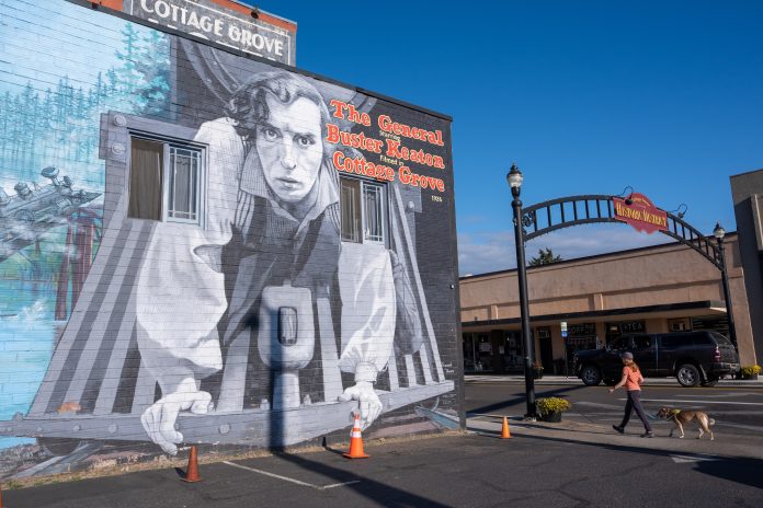 A woman walks her dog near a mural depicting Buster Keaton from his 1926 film, The General, in Cottage Grove, Ore. Fans gathered in the town to celebrate the film