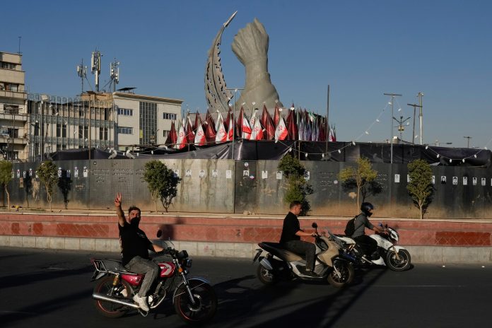 A man reacts to the camera while driving past a monument depicting the clenched fist of the late Iranian Supreme Leader Ayatollah Ali Khamenei, who was killed in U.S. and Israeli strikes on Feb. 28, and a missile at the Islamic Revolution square in downtown Tehran, Iran, Tuesday.