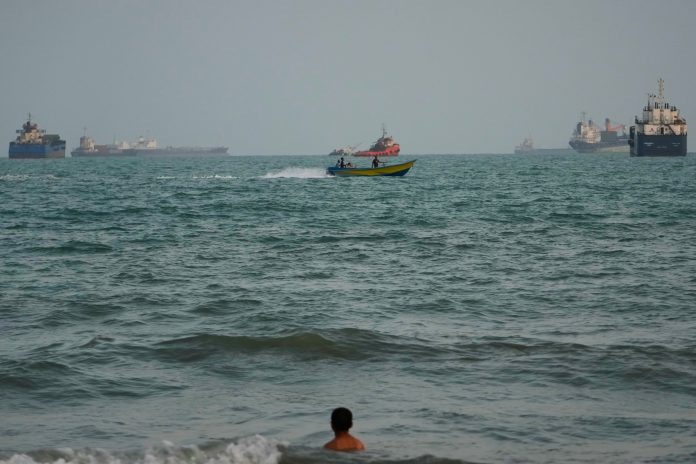 A swimmer remains near the shore as a motorboat passes commercial vessels anchored in the Strait of Hormuz off Bandar Abbas, Iran, on Friday.