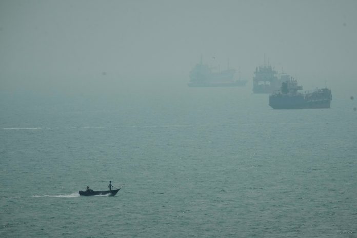 A motorboat travels past commercial vessels anchored amid haze in the Strait of Hormuz off Bandar Abbas, Iran, Monday, Sept. 7, 2026.