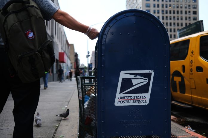 A person drops mail into a blue U.S. Postal Service collection box in New York City in 2020.