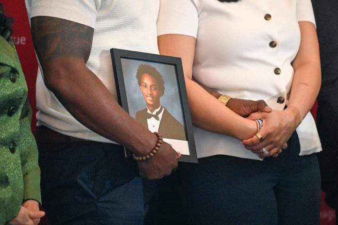 Christine Wonsley and Elmore Wonsley, mother and stepfather of Nolan Wells, stand on a stage with a photo of their son as they appear at the National Urban League